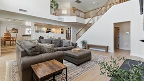 A spacious living area with a large sofa, ottoman, and coffee table, a staircase, and a kitchen in the background. - Splash Canyon - Splash Pad & Tons of Games - Gym (Chandler)