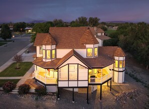 A two-story house with a wrap-around porch, a tower on the right, and a garage on the left.