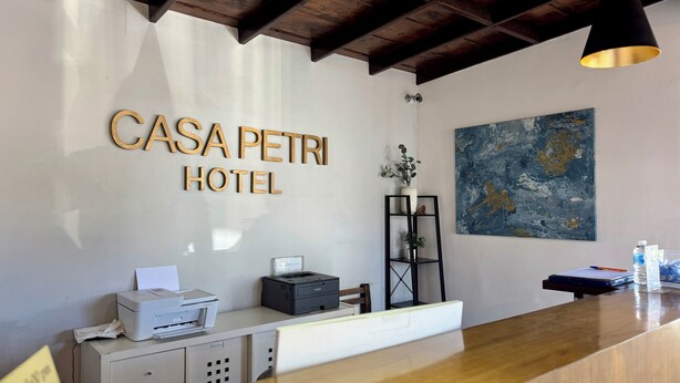 Una recepción con un cartel que dice "CASA PETRI HOTEL", una impresora, una planta y un cuadro en la pared.