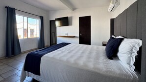 Una habitación de hotel moderna con una cama grande, un televisor de pantalla plana en la pared, una puerta y una ventana con cortinas.