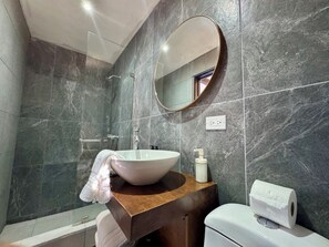 Un baño con un lavabo blanco, un espejo redondo, una toalla, un inodoro y un rollo de papel higiénico.