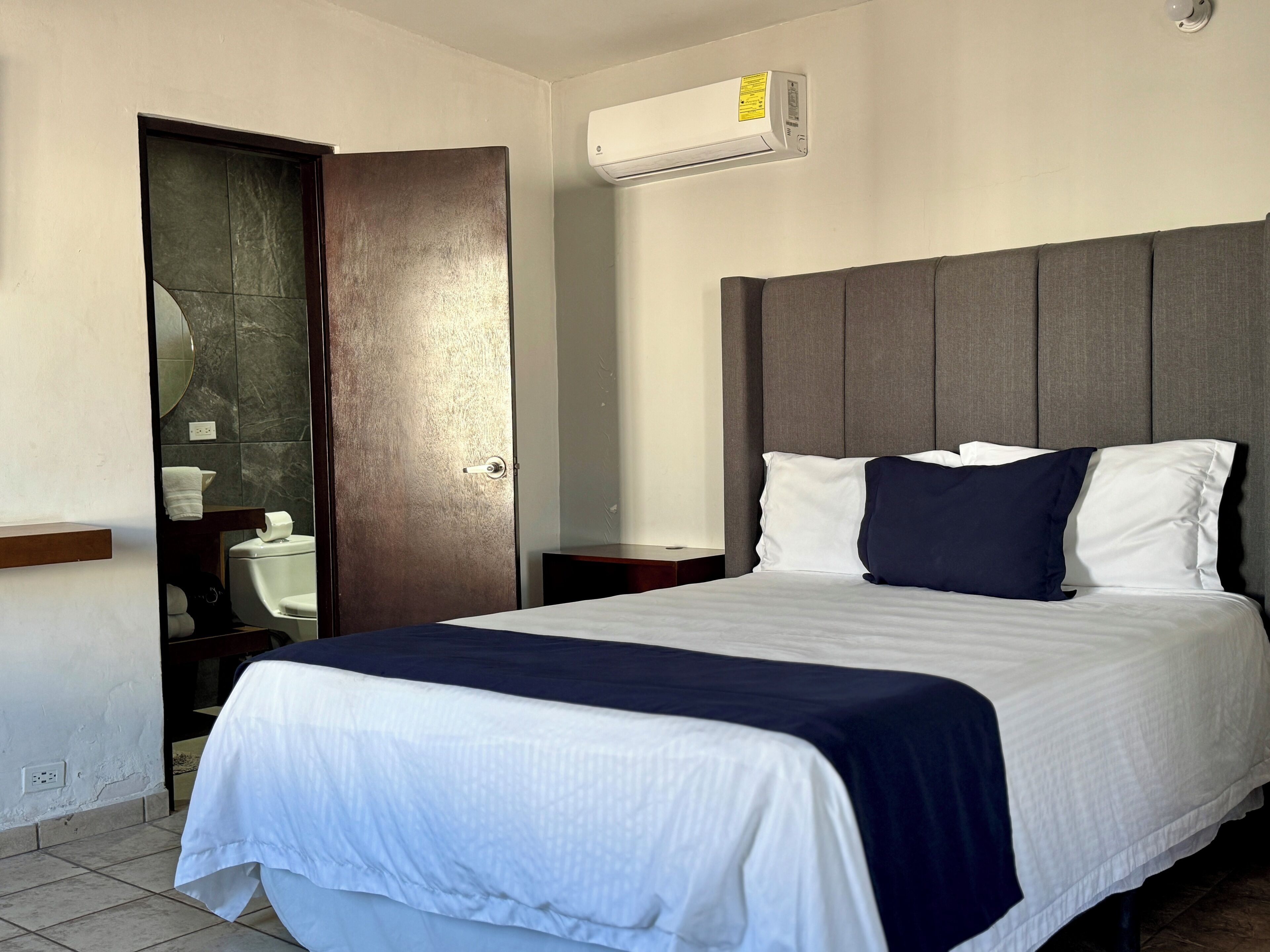 A hotel room with a bed, a bathroom, and an air conditioning unit.