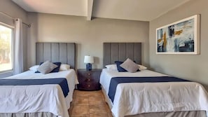Habitación de hotel con dos camas, una mesita de noche, una lámpara y un cuadro en la pared.