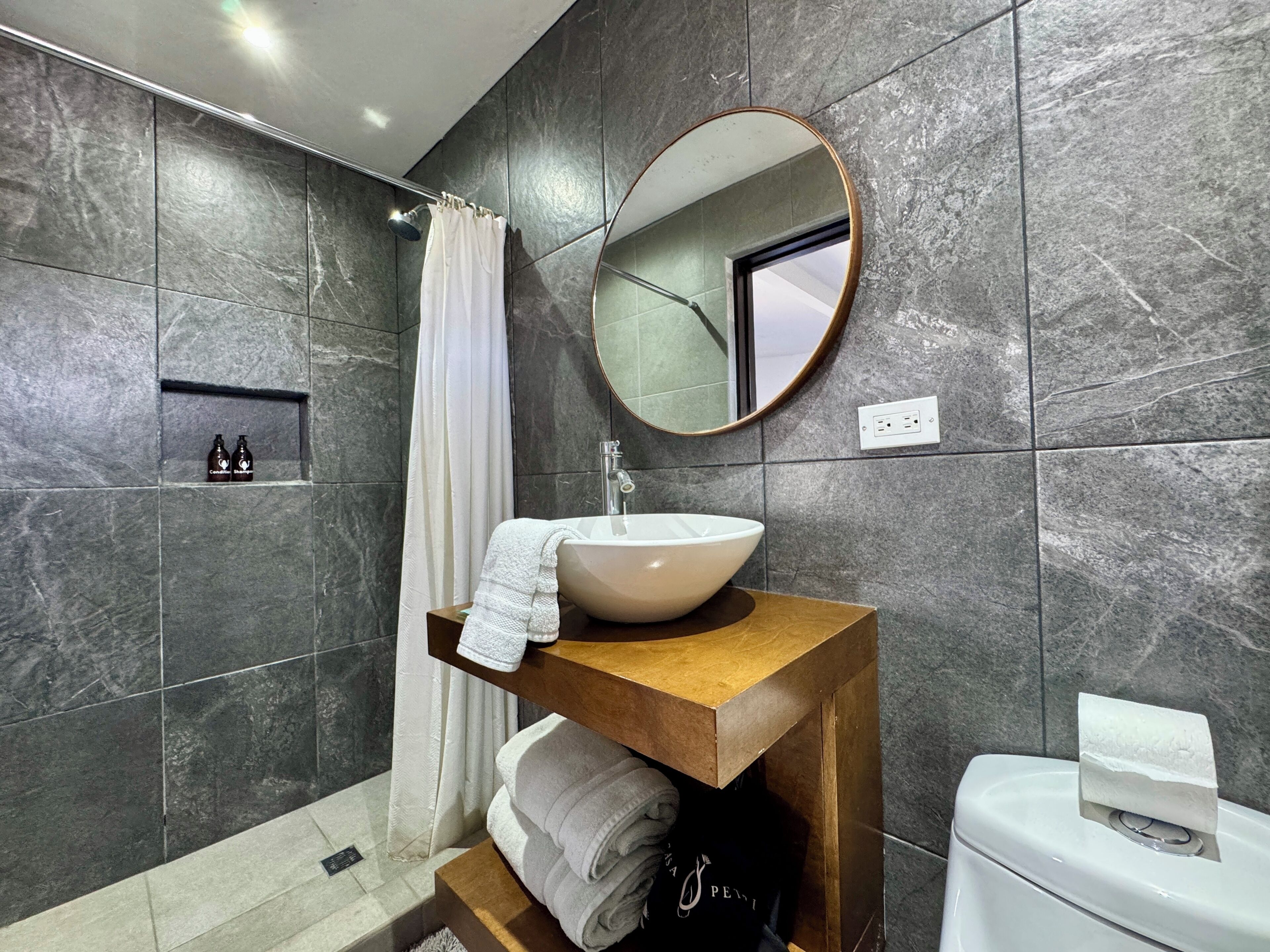A modern bathroom with a large mirror, a vessel sink, a wooden vanity, and a shower area.