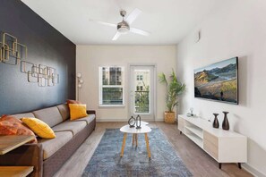 A modern living room with a sofa, a coffee table, a ceiling fan, a painting, and a window with blinds. - Contemporary Stay 10 min to Parks Pets Friendly (Bay Lake)
