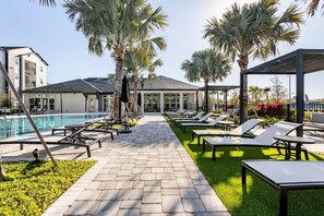 A poolside area with lounge chairs, palm trees, and a clear sky.