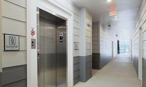 A hallway with an elevator, emergency exit sign, and a door with a wheelchair accessibility symbol.
