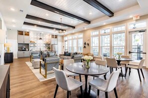 A modern hotel lobby with a dining area, sofas, and a kitchen in the background.