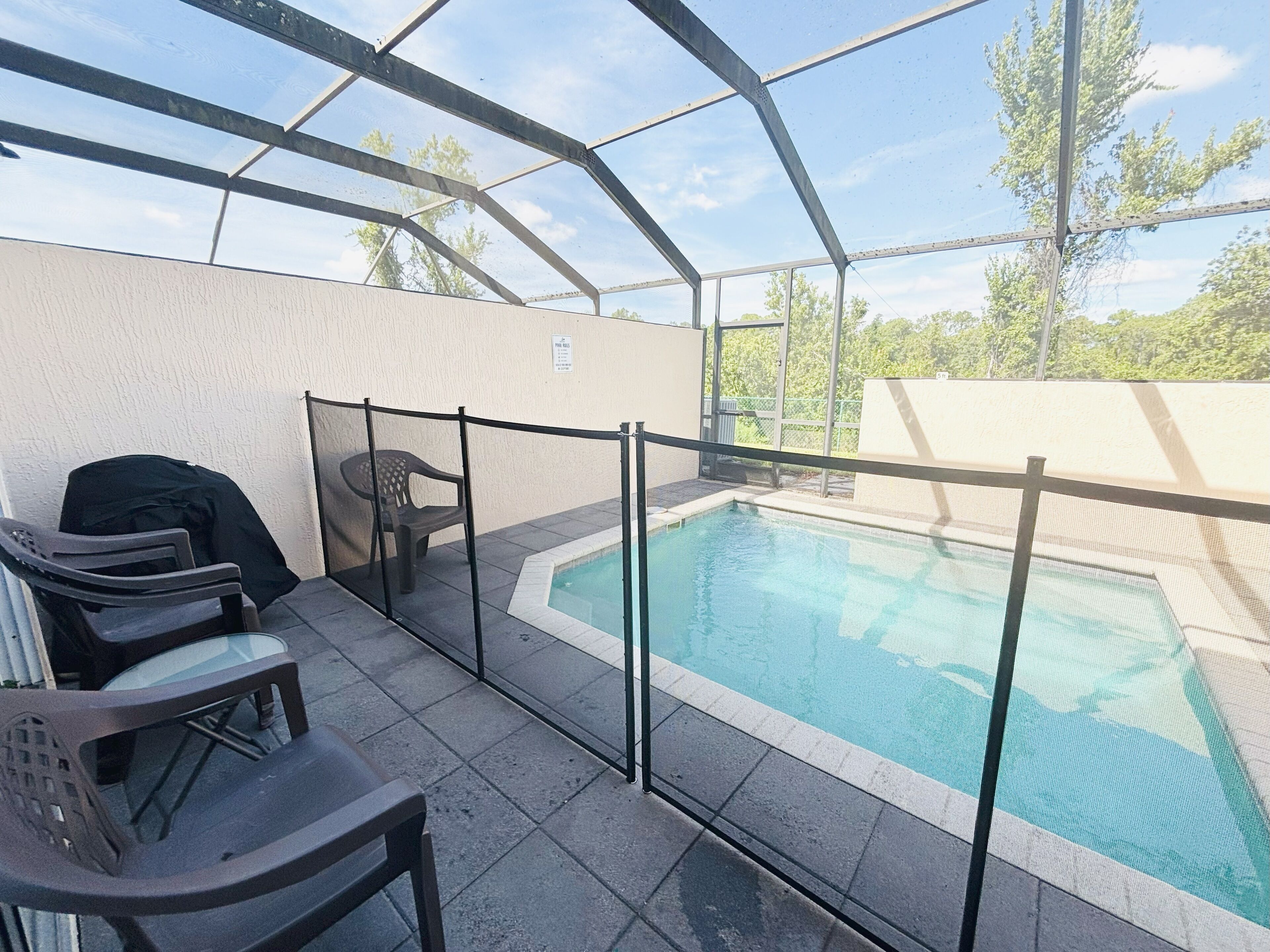 Zona de piscina exterior con cerramiento de vidrio, mobiliario y una parrilla cubierta.