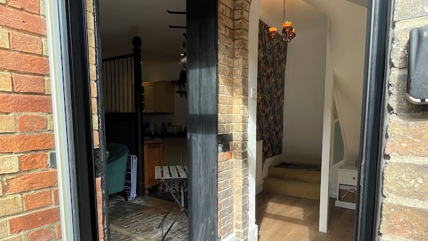An interior view of a home with a brick exterior, a wooden floor, and a kitchen area visible through an open door.