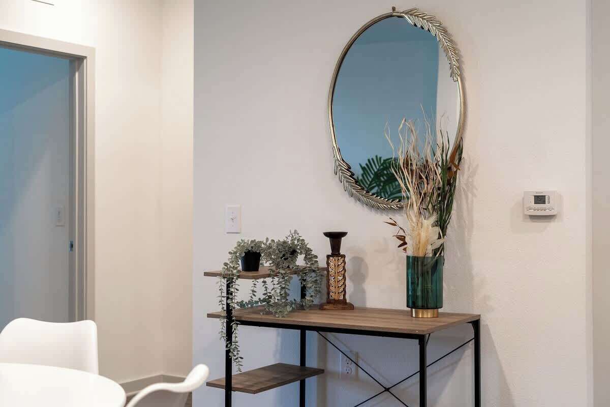 A room with a white chair, a wooden console table with decorative items, a mirror, and a door.