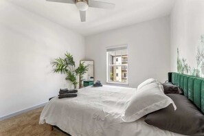 A bedroom with a bed, a ceiling fan, a window, and a green upholstered headboard.
