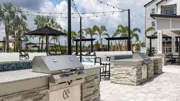 Un espace extérieur avec une piscine, un barbecue, des chaises longues et des parasols.