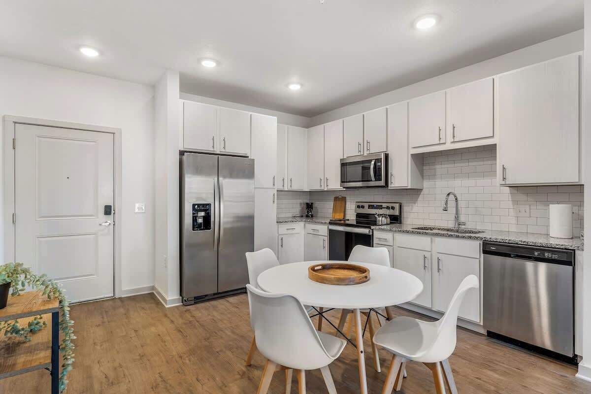 A modern kitchen with white cabinets, stainless steel appliances, and a round dining table with white chairs.