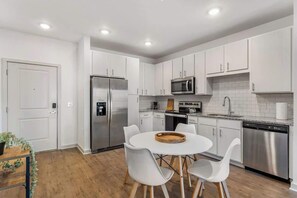 A modern kitchen with white cabinets, stainless steel appliances, and a round dining table with white chairs.