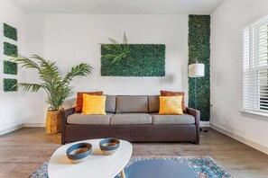 A modern living room with a grey sofa, decorative pillows, a potted plant, a white coffee table with bowls, and a patterned rug.