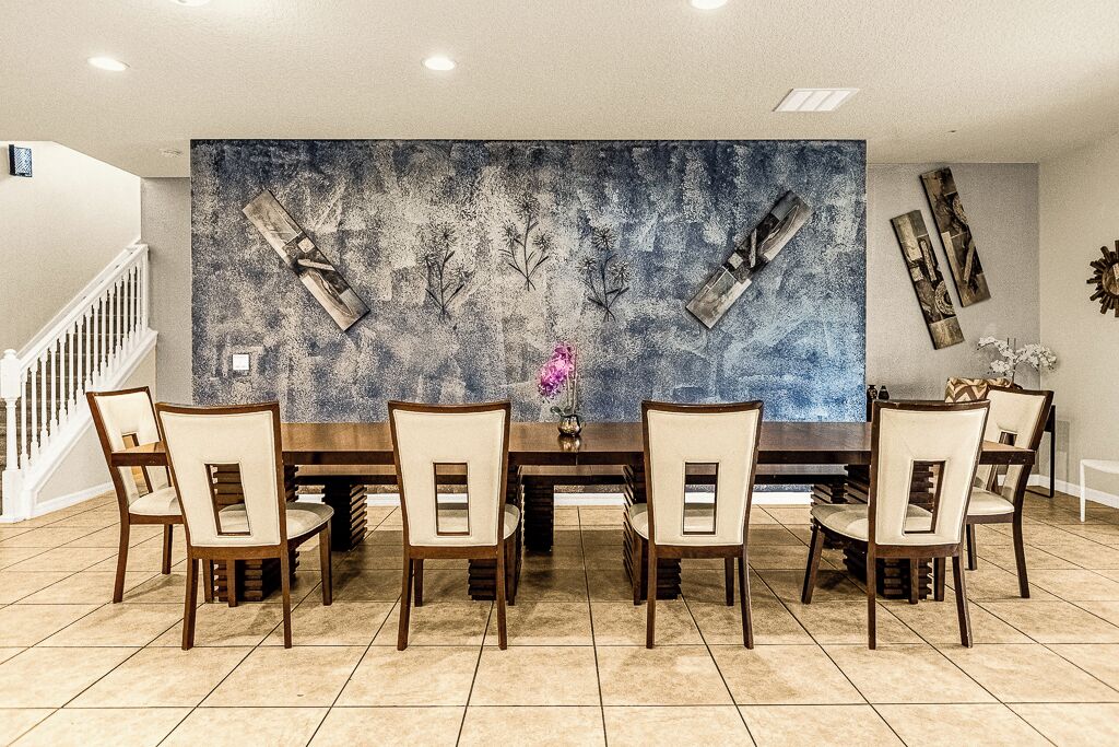 Un espace repas comprenant une grande table, six chaises et un mur décoratif orné d’œuvres d’art abstraites.
