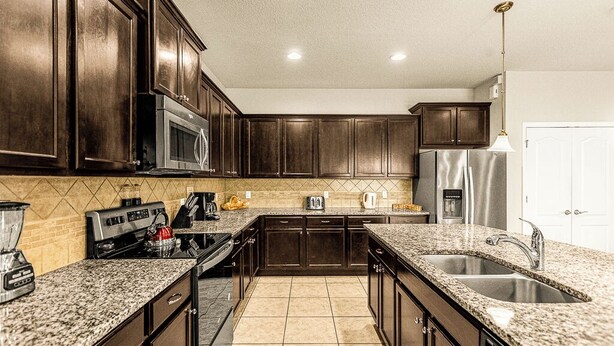Una cocina con gabinetes de madera oscura, encimeras de granito y un refrigerador de acero inoxidable, además de un microondas integrado.