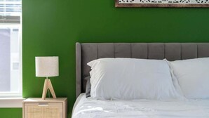 Ein Bett mit weißer Bettwäsche, einem grauen Kopfteil und einem Nachttisch mit Lampe und Radio.