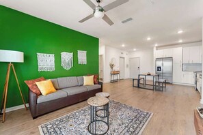 A modern living room with a green accent wall, a sofa, a coffee table, and a ceiling fan. - Cozy 2Bed Boho Hideaway 10 Min to Parks Allows Pet (Bay Lake)