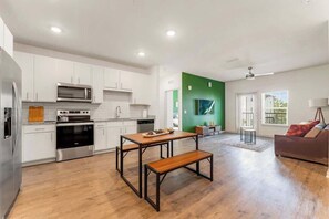 A modern kitchen with white cabinets, a stainless steel oven, and a wooden dining table with benches. - Cozy 2Bed Boho Hideaway 10 Min to Parks Allows Pet (Bay Lake)