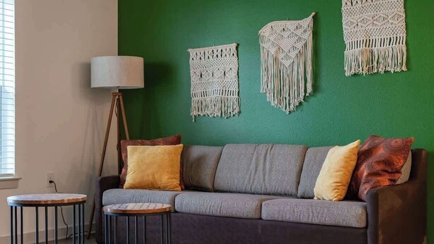 A room with a green wall, a grey sofa with cushions, a floor lamp, and two round tables. - Cozy 2Bed Boho Hideaway 10 Min to Parks Allows Pet (Bay Lake)