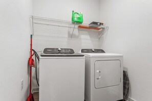 A laundry area with two washing machines, a drying rack, and a green bottle on a shelf.