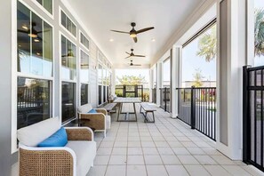 Une terrasse extérieure couverte, dotée de sièges, de ventilateurs de plafond et de grandes fenêtres.