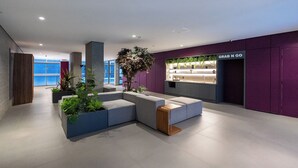 A modern lobby with a grey sectional sofa, potted plants, and a 'Grab N Go' counter.