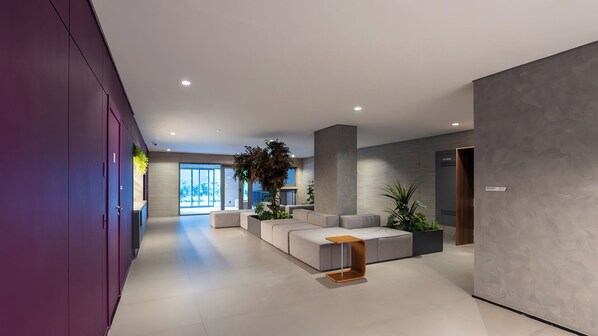 A modern reception area with a grey sofa, a wooden coffee table, and a large plant. - On Domingos de Morais (São Paulo)