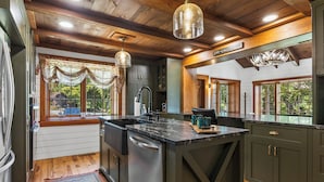 A kitchen with wooden ceiling beams, a central island, and a view of the outdoors through large windows. - Grand Shore Haven (Lake George)