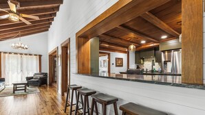 A spacious kitchen with wooden beams, a bar area with stools, and a view into the dining room. - Grand Shore Haven (Lake George)
