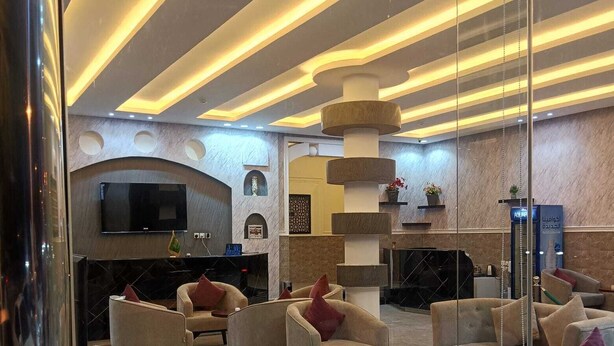 A modern lobby with a TV, sofas, a fireplace, and a decorative pillar. - Lailati Alnahda (Riyadh)