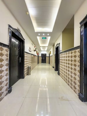Un pasillo de hotel con piso de baldosas, puertas negras, azulejos decorativos en la pared e iluminación empotrada en el techo.