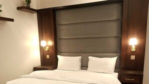 A neatly arranged bedroom with a large bed, two bedside tables with lamps, a grey armchair, and a wooden bedside table with a remote control. - Lailati Alnahda (Riyadh)