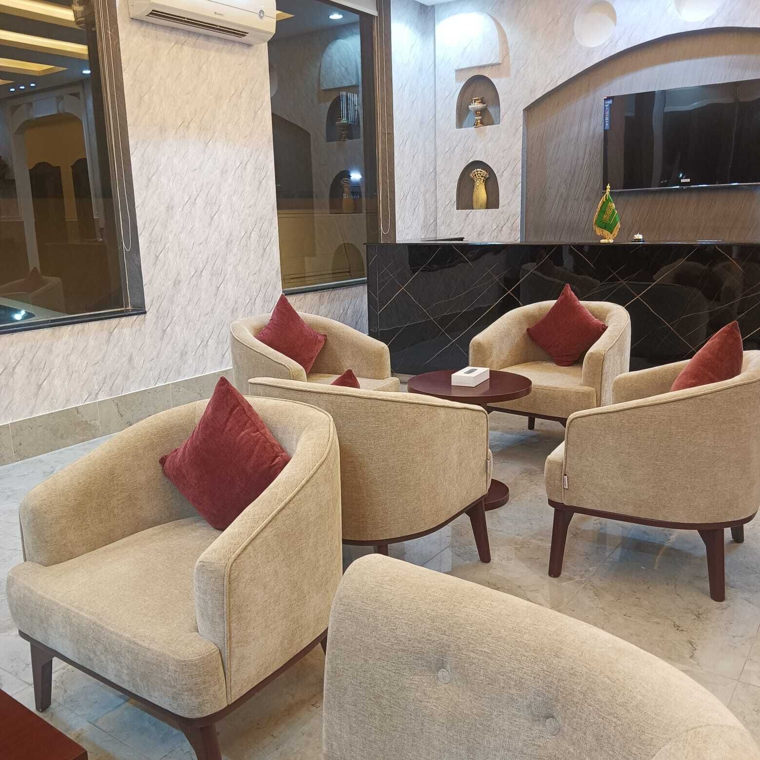 A modern lounge area with beige armchairs and a round table, marble walls, and a black tiled backsplash.