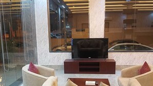 A lobby with a TV, seating area, and a glass wall reflecting the outside. - Lailati Alnahda (Riyadh)