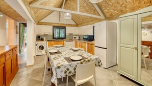 A compact kitchen with wooden beams, a dining table set for four, a washing machine, and a refrigerator. - Small Creole Kaz with garden and jacuzzi, near Grande Anse beach (Petite-Île)