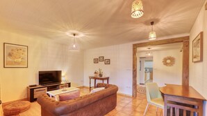 A living room with a brown sofa, a coffee table, a TV, and two pendant lights. - Small Creole Kaz with garden and jacuzzi, near Grande Anse beach (Petite-Île)