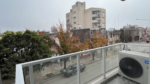 A balcony with a view of a cityscape, including buildings and a street with a parked vehicle. - Esmeralda Apart (Marcos Juárez)