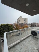 Un balcón con vista a un paisaje urbano, incluyendo edificios y una calle con un vehículo estacionado.