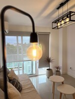 Una sala de estar moderna con un ventanal grande, un sofá, dos mesitas auxiliares y una lámpara colgante.