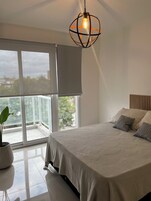 Un dormitorio con cama, planta en maceta, un ventanal con vistas y una lámpara colgante.