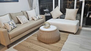 Ein Wohnzimmer mit einem beigen Sofa, einem weißen Sessel und einem gewebten Hocker.