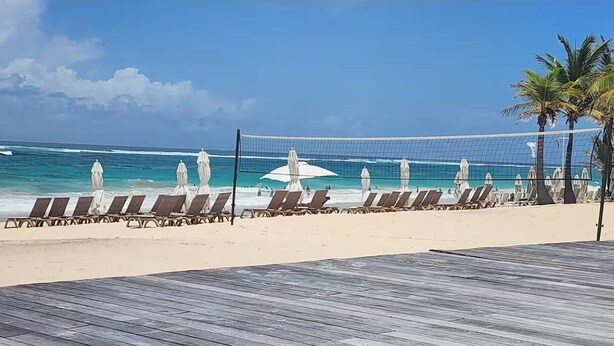 Ein Strand mit Volleyballnetz, Liegestühlen und Sonnenschirmen.