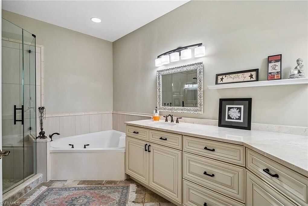 A bathroom with a bathtub, vanity with drawers, a large mirror, and a shower area.