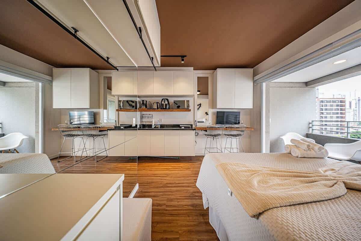 Una habitación de hotel moderna con kitchenette, una cama con manta, un escritorio y una silla.