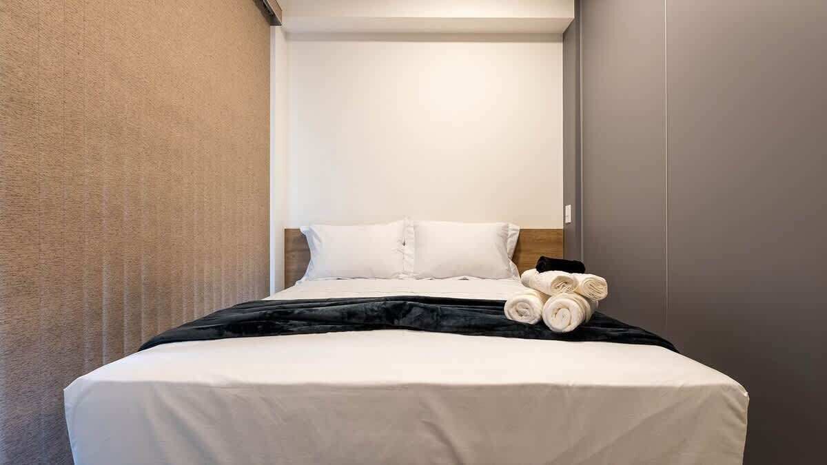 A neatly made bed with white linens, a black blanket, and rolled towels on the side.