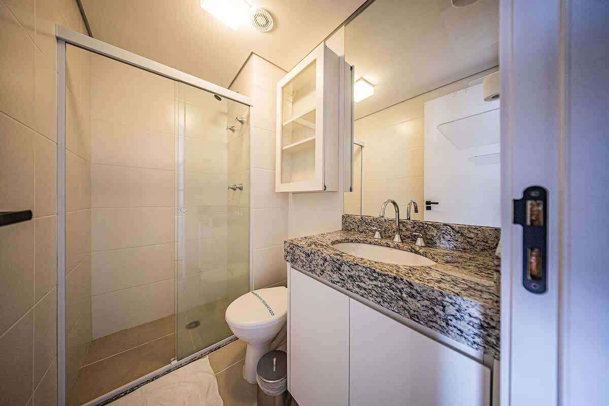 A bathroom with a glass shower enclosure, a white toilet, a granite countertop sink, and a white cabinet.