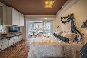 A modern bedroom with a large bed, a desk with a computer, and a view of the city through large windows. - Mode Perdizes (São Paulo)